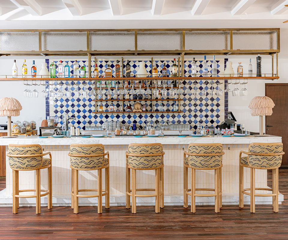 Blu Beach Bar & Grill – Four Seasons Hotel Tunis Five light wood James Bar Chairs with patterned fabric seats arranged in front of a bright marble counter at Blu Beach Bar & Grill.
