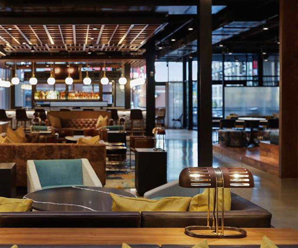 Canopy by Hilton Memphis Downtown The Turing Table Lamp sitting turned on on a wooden surface in a spacious, modern hotel lounge or restaurant interior at Canopy by Hilton Memphis Downtown.