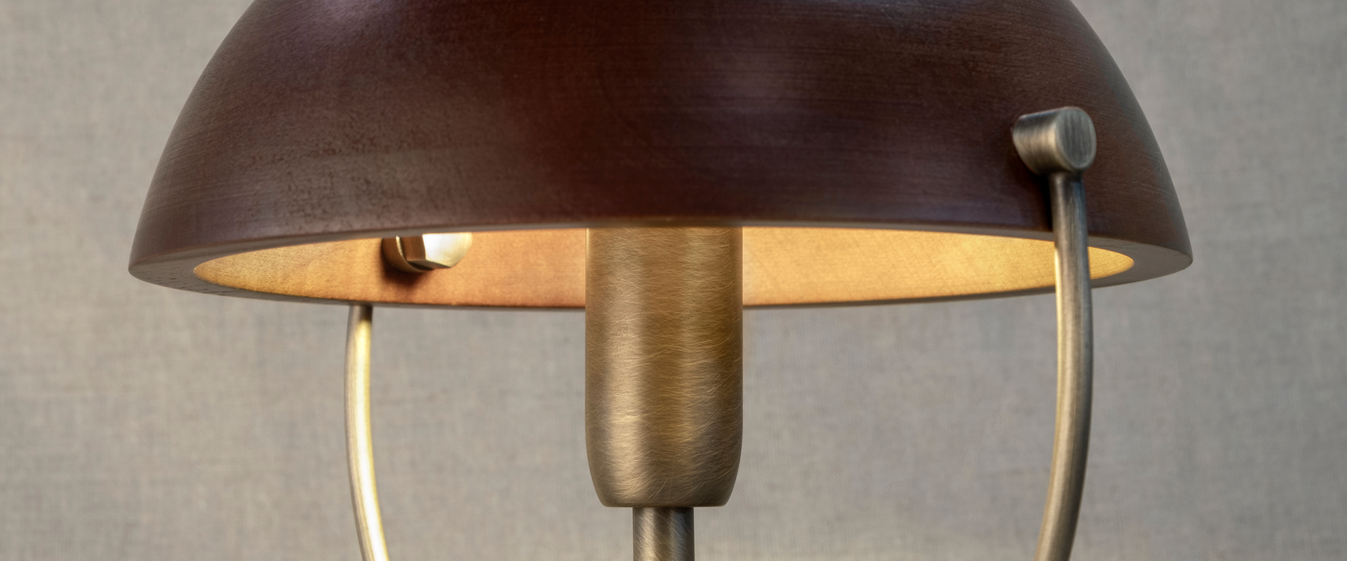 Faraday Wall Lamp Close-up of the Faraday Wall Lamp by Wood Tailors Club, showcasing the interior of its smoked walnut domed shade softly illuminated, revealing the aged brushed brass socket and metal ring structure.