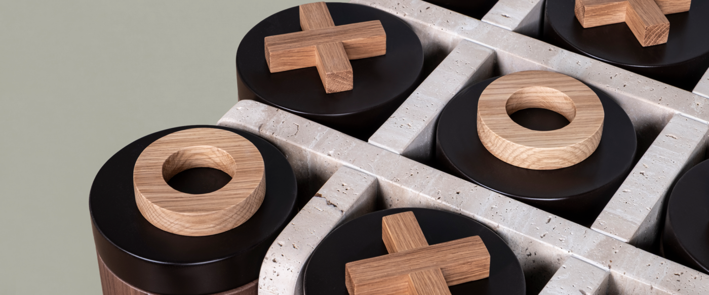 Close-up of the Kensington Tic-Tac-Toe table by Wood Tailors, showing oak X and O pieces on black lacquered lids, set within a travertine grid.