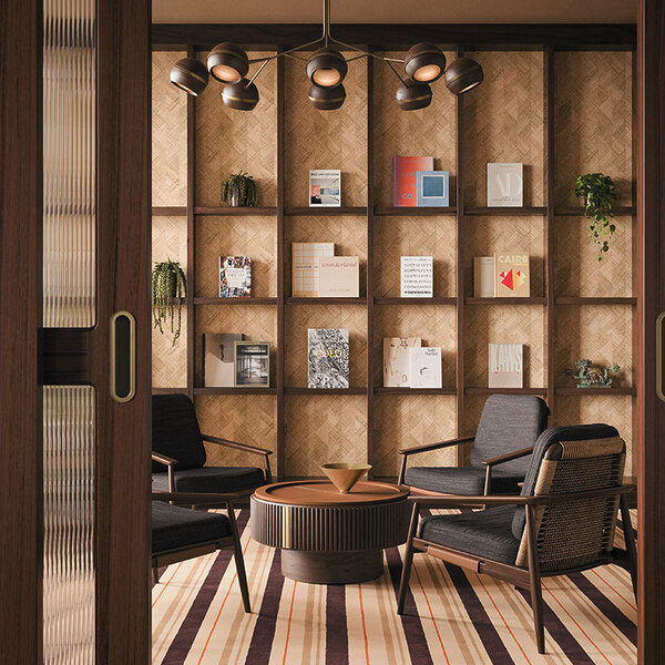 Four Adam Armchairs upholstered in black fabric with rattan details arranged in a circle around a Robert center table in smoked walnut wood with leather and brushed brass accents. The living room is warmly lit, featuring a bookcase backdrop illuminated by a Fleming suspension lamp, framed by two fluted glass doors.