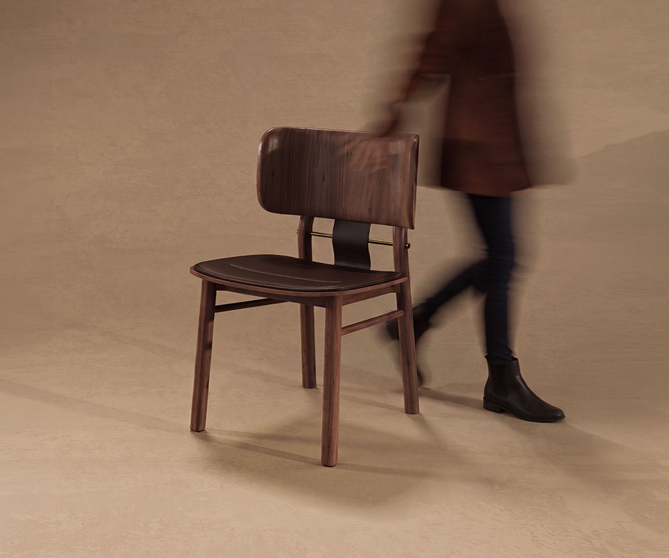 Arthur Dining Chair Three-quarter front view of the Arthur Dining Chair in a warm studio setting, with a motion-blurred person walking past in the background.