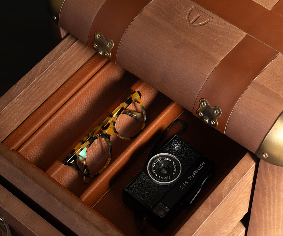 Close-up of the Burke side table showcasing the drawers’ leather interior with a vintage camera and glasses inside. The tabletop features the Wood Tailors Club brand icon engraved in the wood.