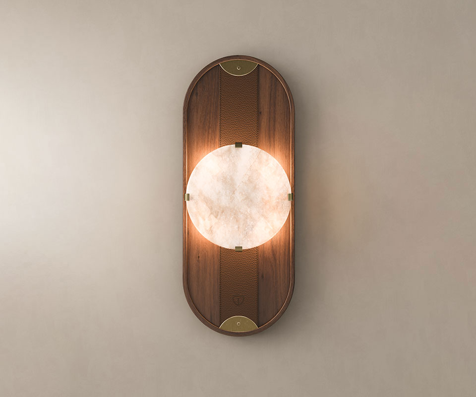 Cavendish Wall Lamp Cavendish Wall Lamp, front view, with the light turned on. Crafted from smoked walnut wood and alabaster, framed in a gentle oval silhouette with aged brushed brass accents, showcasing the lamp’s refined materials and elegant design set against a beige wall.