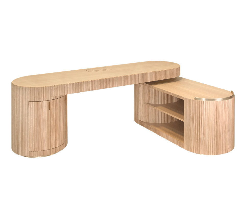 Gifford desk by Wood Tailors Club in oak. An angled perspective view of the desk in an L-shaped arrangement. It features an oak fluted-panel cabinet on the left, supporting the main oak top, and a lower oak shelf module with two open shelves extended to the right, finished with a brass trim.