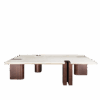 A wide front view of the Grenville Center Table featuring a thick, rectangular cream travertine top. The structure consists of four chunky, asymmetrical legs made of dark smoked walnut wood. One leg features a distinctive vertical U-shaped cutout that notches into the stone top, revealing a thin brushed brass inlay along the edge.