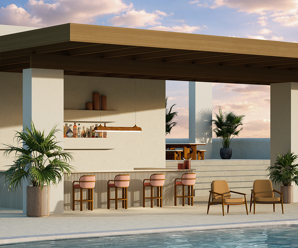 Outdoor living: A luxurious outdoor poolside lounge featuring handcrafted teak wood furniture by Wood Tailors Club. In the foreground, two Adam armchairs with tan upholstery sit beside a sparkling blue pool. Behind them, a fluted bar is lined with four James bar chairs featuring pink curved backrests. Above the bar hangs the sleek, linear Bruce suspension lamp. In the background, the Portman dining set is visible on a raised terrace under a modern pergola, all set against a serene sunset sky and tropical greenery.