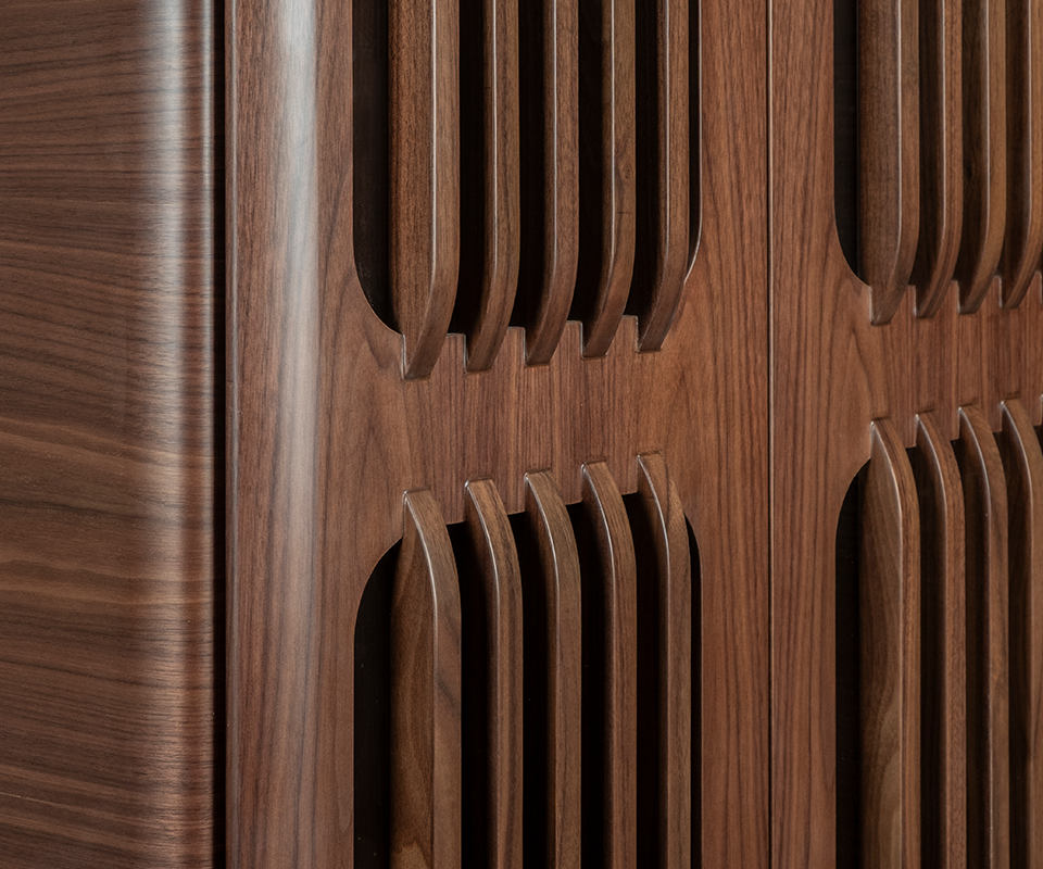 A macro detail shot focusing on the craftsmanship of the slatted door panels in smoked walnut wood, showcasing the smooth joinery where the vertical slats meet the solid wood frame.