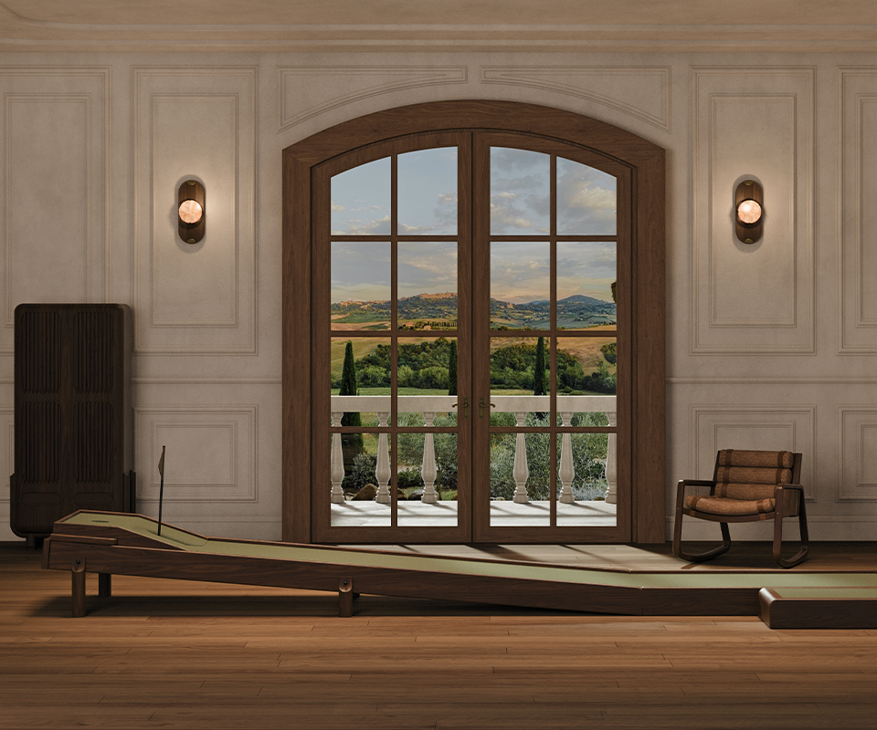 An interior lifestyle scene showing the Sutherland Mini Golf set placed in a luxury room with classic wall moldings and large arched French doors overlooking a scenic landscape.