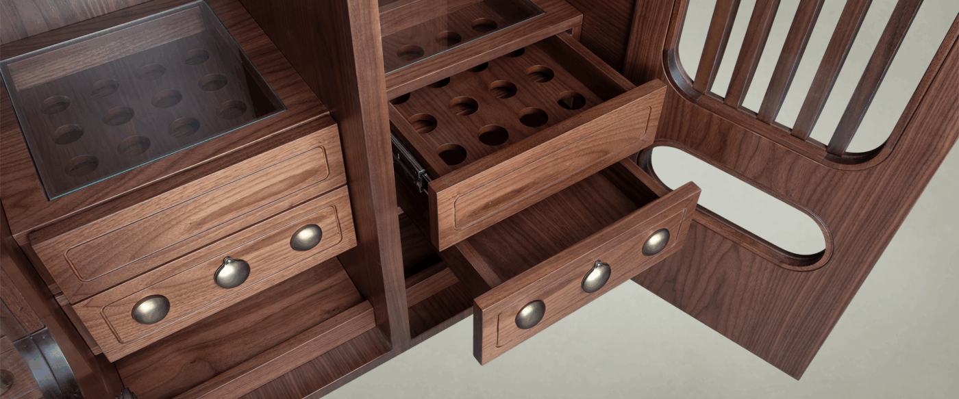 A high-angle close-up of the internal drawer system in smoked walnut wood. The image shows one drawer partially extended, revealing a bespoke wooden grid with circular cutouts designed to hold golf balls. The drawers are finished with spherical aged brushed brass details, and the top compartments are covered with protective glass panels.