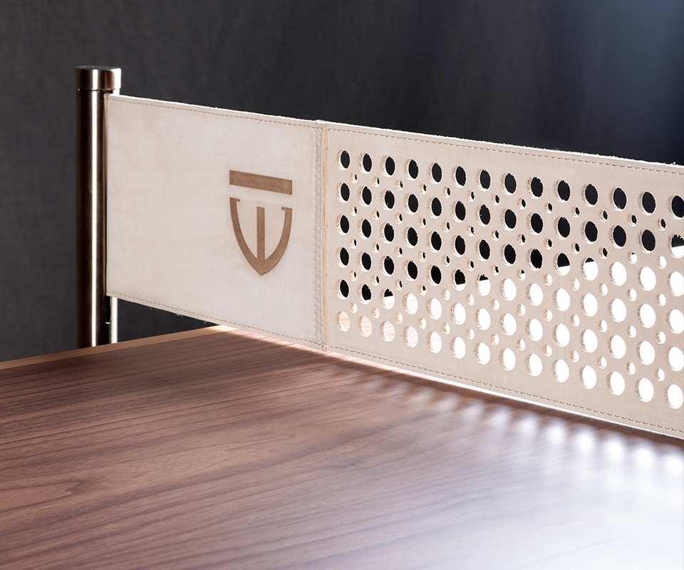 Keppel Ping-Pong Table Detailed close-up of a luxury ping pong table made of smooth walnut wood, featuring a custom off-white perforated leather net with the Wood Tailors Club crest embossed on the side, anchored by a sleek stainless steel post.