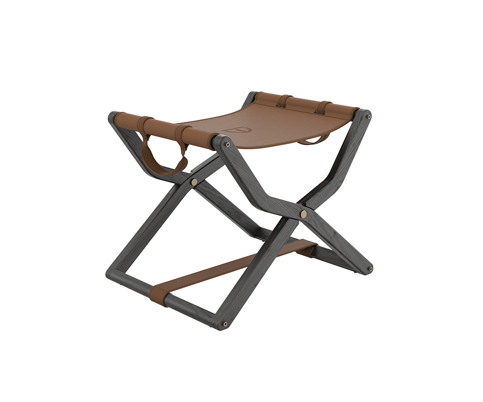 Three-quarter view of the Korda Folding Stool featuring a dark, stained wood frame and a rich cognac leather seat with gold-toned metallic hardware.