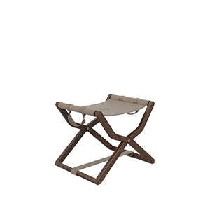 Three-quarter view of the Korda Folding Stool showcasing a walnut wood frame with a rich, deep finish. The design features a beige leather sling seat with elegant strap details and metallic accents, embodying a sophisticated, modern silhouette.