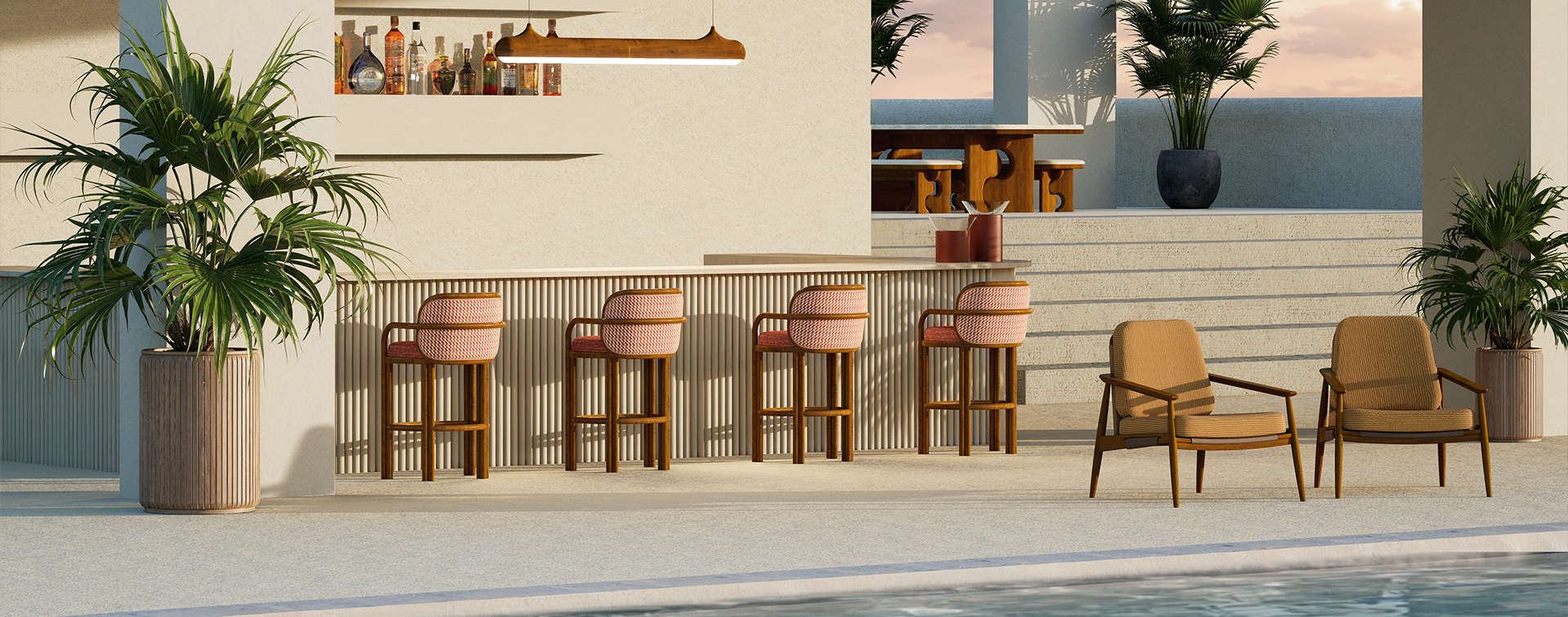Outdoor living: A luxurious outdoor poolside lounge featuring handcrafted teak wood furniture by Wood Tailors Club. In the foreground, two Adam armchairs with tan upholstery sit beside a sparkling blue pool. Behind them, a fluted bar is lined with four James bar chairs featuring pink curved backrests. Above the bar hangs the sleek, linear Bruce suspension lamp. In the background, the Portman dining set is visible on a raised terrace under a modern pergola, all set against a serene sunset sky and tropical greenery.