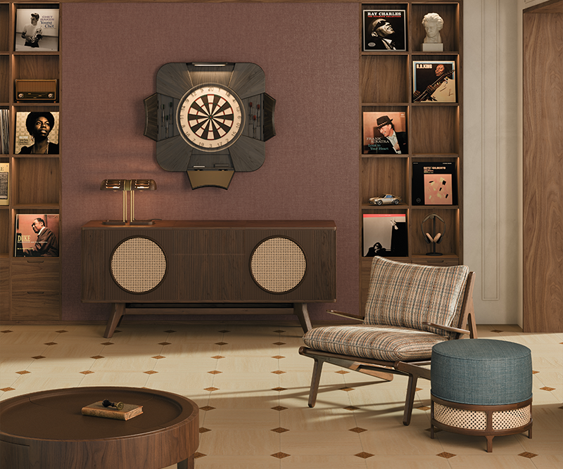 A serene living room bathed in soft daylight from the window, featuring the open Rochford dartboard by Wood Tailors Club in black-stained ash wood with powder coated stainless steel details. The scene includes the Harrison sideboard, a Turing table lamp glowing gently above, a Moore armchair in textured fabric, and the George stool, creating a harmonious and refined interior.