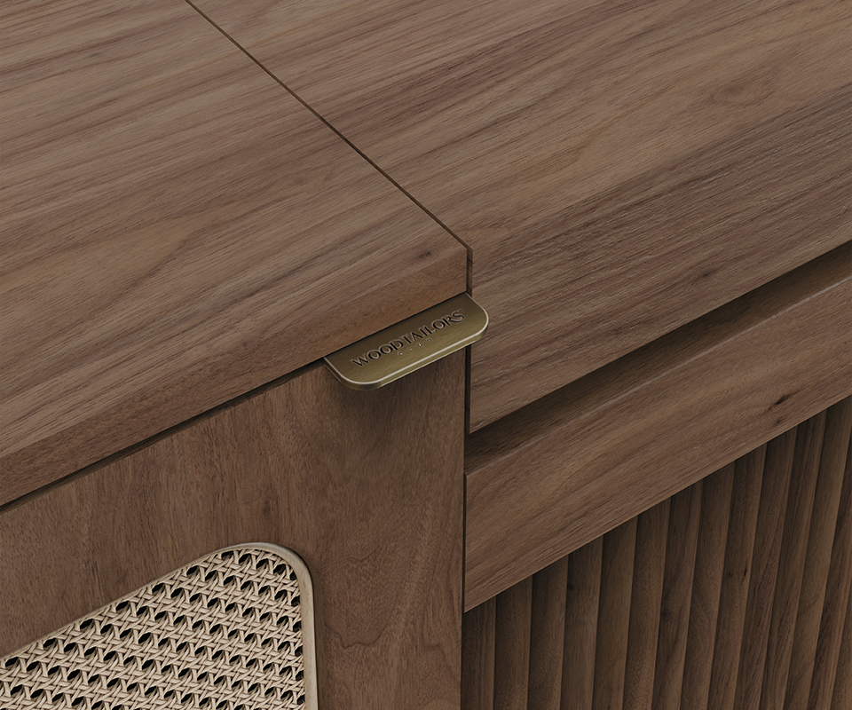 Close-up angle showing a brass handle engraved with "Wood Tailors", wood grain top, rattan woven cane door, and slatted front panel.