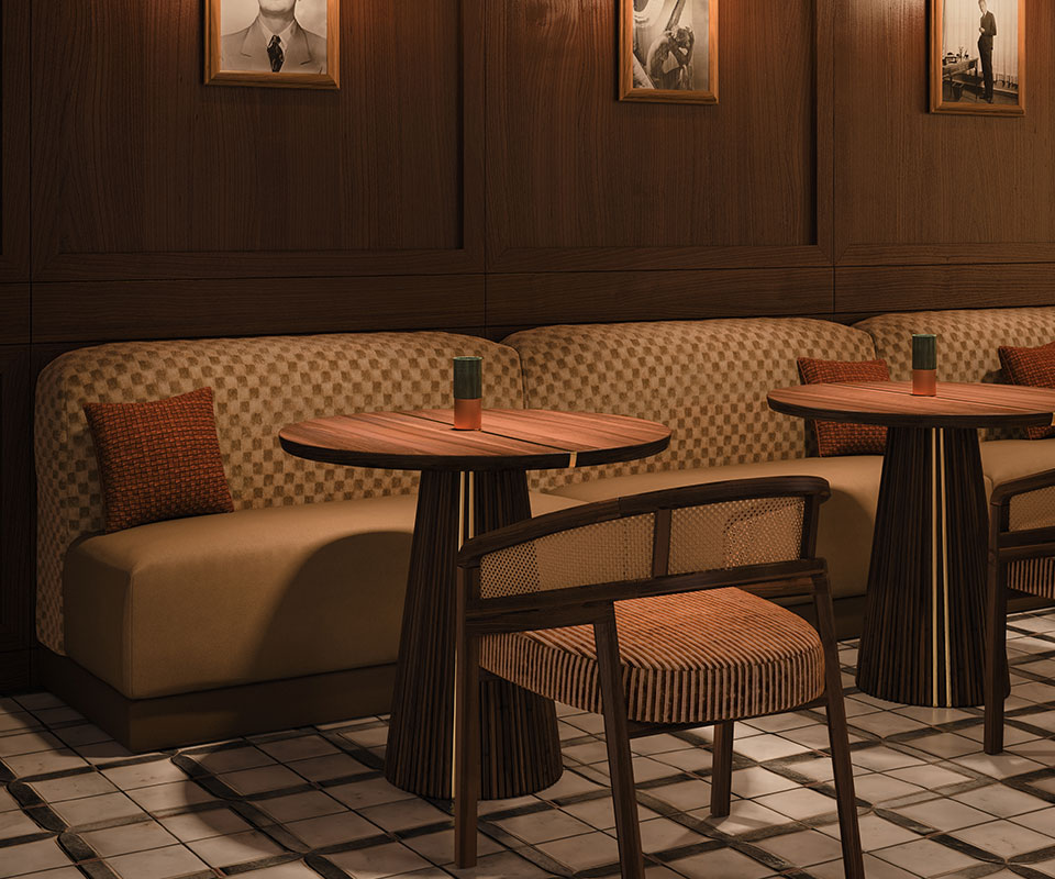 Spencer Dining Chair Spencer dining chair upholstered in striped fabric, with a smoked walnut wood structure and rattan details, in a restaurant setting with mood lighting, next to the Henry dining table.