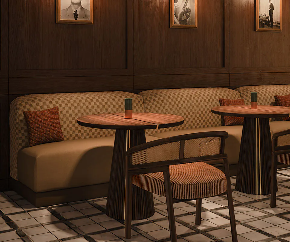 Spencer Dining Chair Spencer dining chair upholstered in striped fabric, with a smoked walnut wood structure and rattan details, in a restaurant setting with mood lighting, next to the Henry dining table.