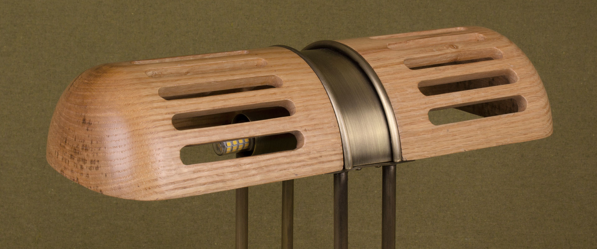 Turing Table Lamp Detail of the Turing Table Lamp shade, crafted in natural oak and aged brushed brass, set against a green background.