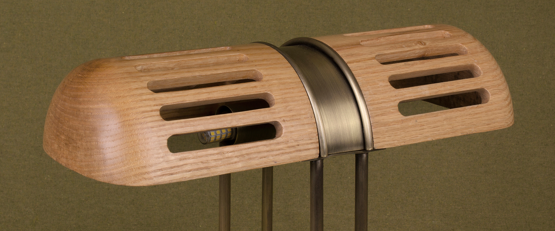 Turing Table Lamp Detail of the Turing Table Lamp shade, crafted in natural oak and aged brushed brass, set against a green background.